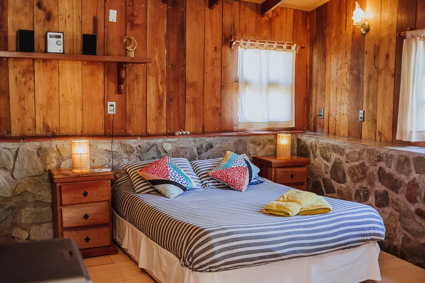 Dormitorio de la cabaña Roble con paredes de madera, zócalo de piedra y cama de plaza y media